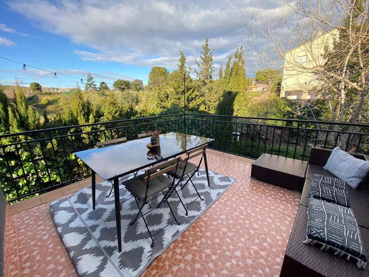 Terrace with a dining table and rattan sofa opening onto open green countryside