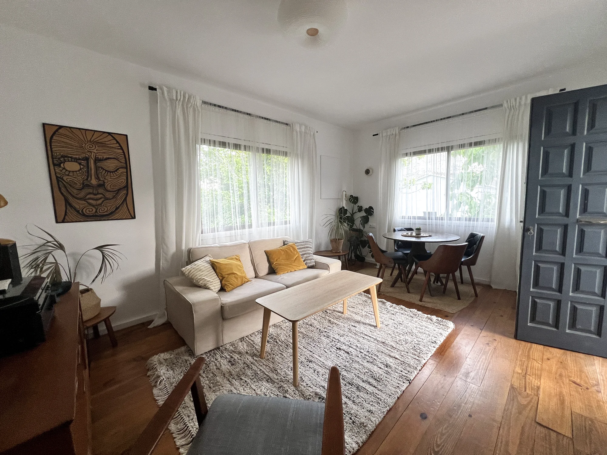 Open living and dining room with a beige sofa, round wooden table and a blue panelled door