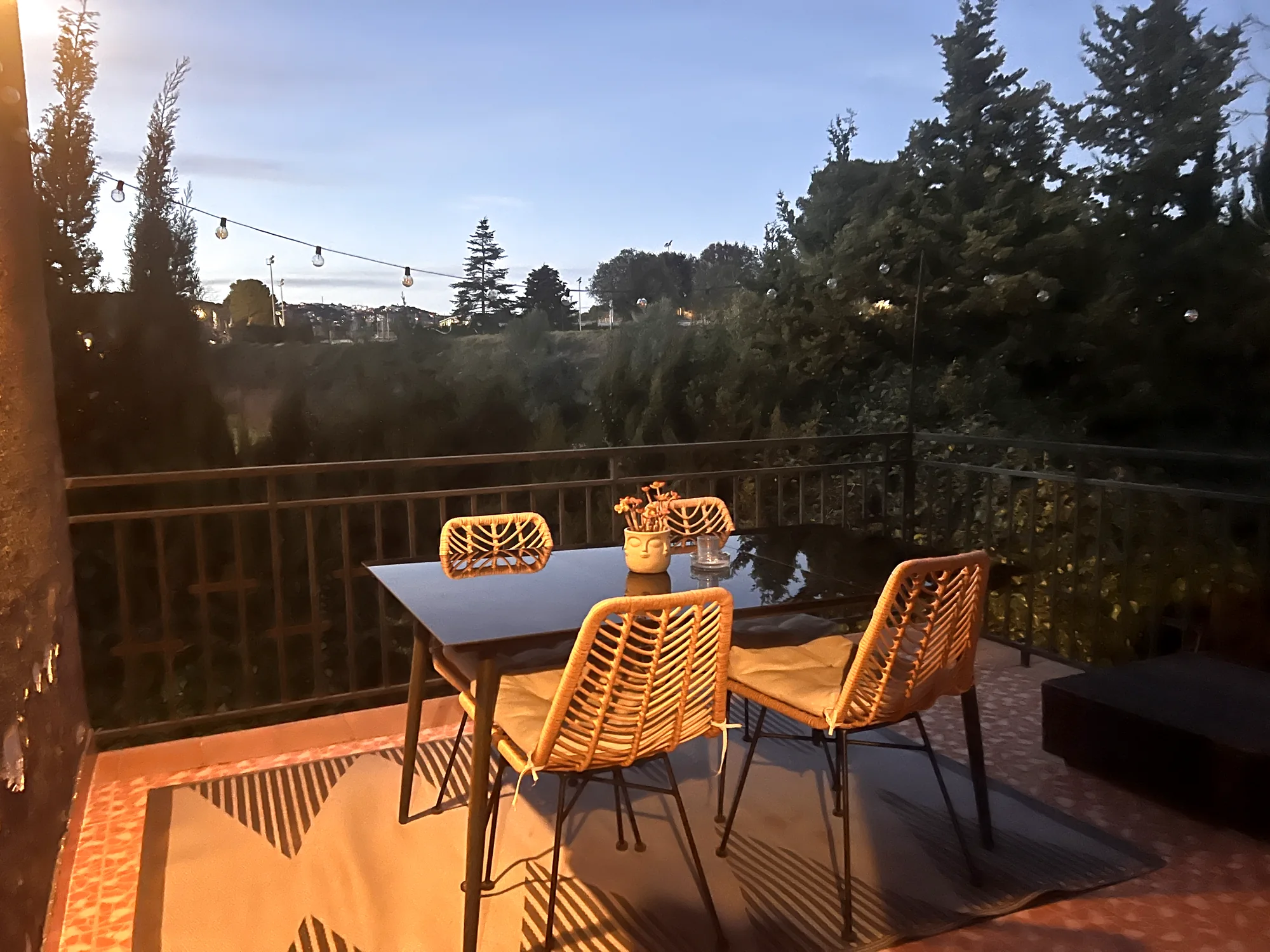 Terrace at dusk with a dining table beneath warm string lights and an open countryside view